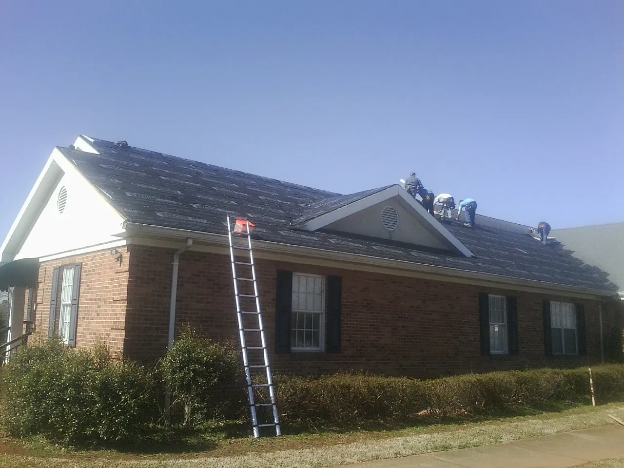 Crew tearing shingles off a brick ranch roof with a ladder set — Metal Roof Repair work by our crew in Chisago City