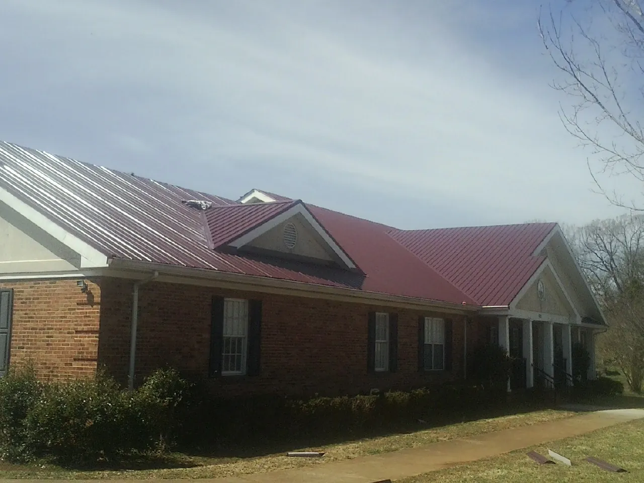 Red metal roof with gabled entries on a long brick building, from a Hail Damage Roof Repair job in Chisago City