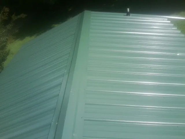 New green metal panels meeting at the ridge of a roof — Flat Roof Repair work by our crew in Chisago City