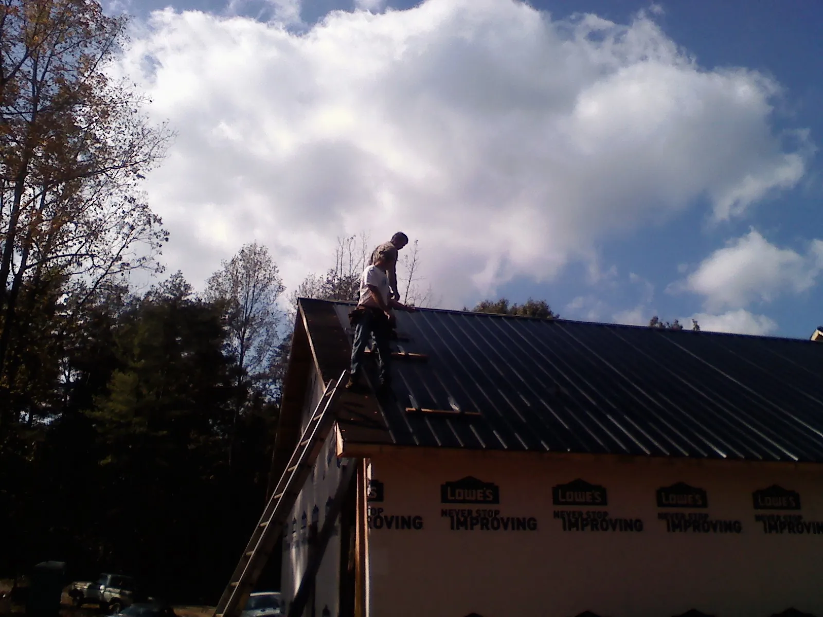 Roofer fastening dark metal panels high against a cloudy sky, from a Roof Inspection job in Chisago City