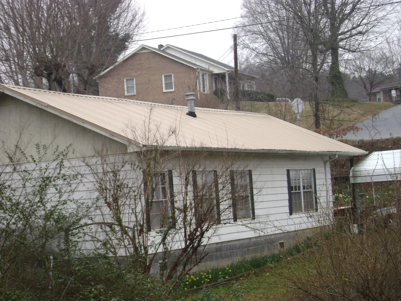 Tan metal roof on a white sided house set into a hillside — Commercial Roofing by Roofing Brothers in Chisago City